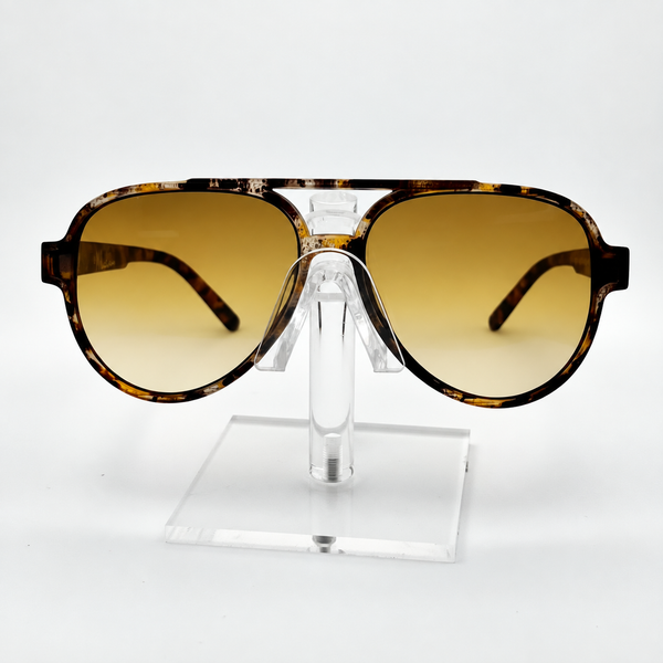 A pair of oversized aviator-style sunglasses with a tortoiseshell frame and gradient amber lenses, displayed on a clear acrylic stand against a white background.
