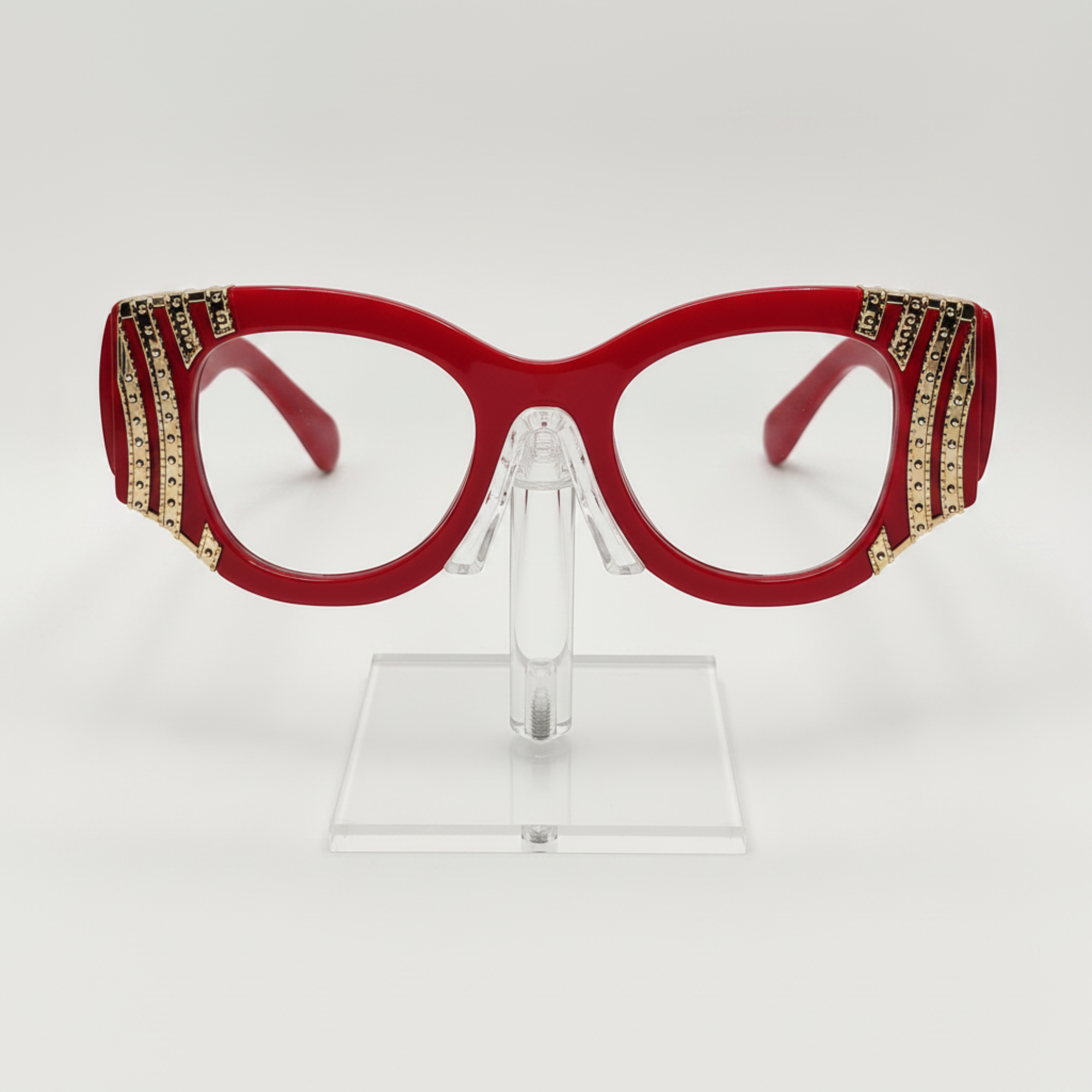 Red cat-eye eyeglasses with gold rhinestone embellishments on the temples, displayed on a clear acrylic stand against a white background.