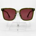 Olive green oversized square sunglasses with dark reddish-brown tinted lenses, displayed on a clear acrylic stand against a white background.