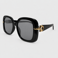 Black oversized square sunglasses with dark gray lenses and gold metal hardware on the temples, shown on a light gray background.
