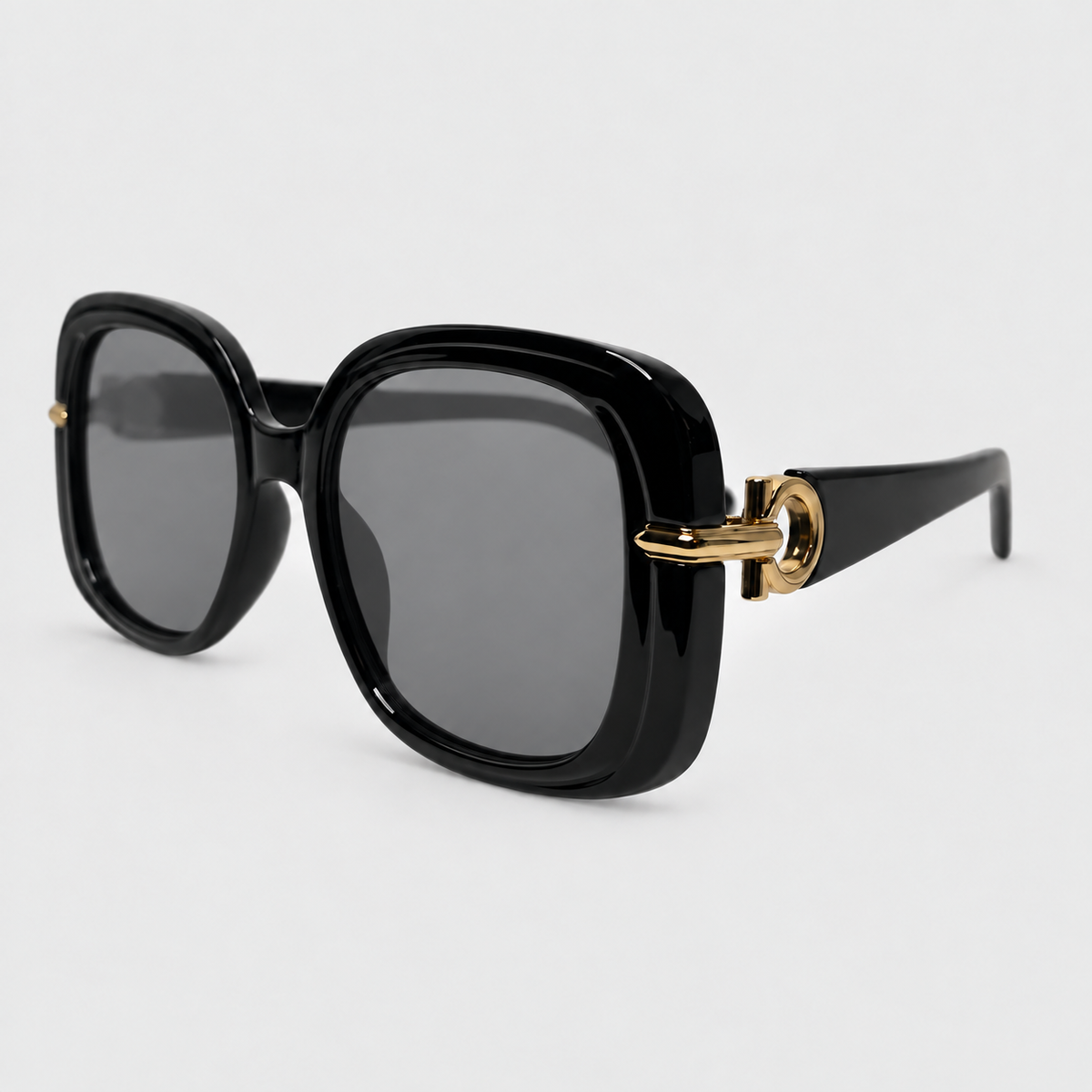 Black oversized square sunglasses with dark gray lenses and gold metal hardware on the temples, shown on a light gray background.