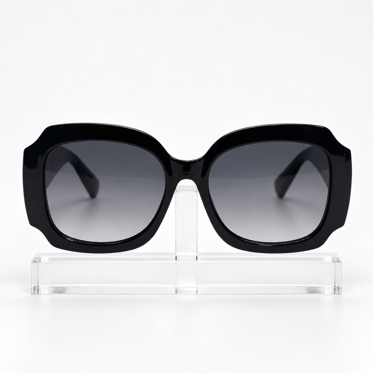 Black oversized square sunglasses with gradient gray lenses, displayed on a clear acrylic stand against a white background.