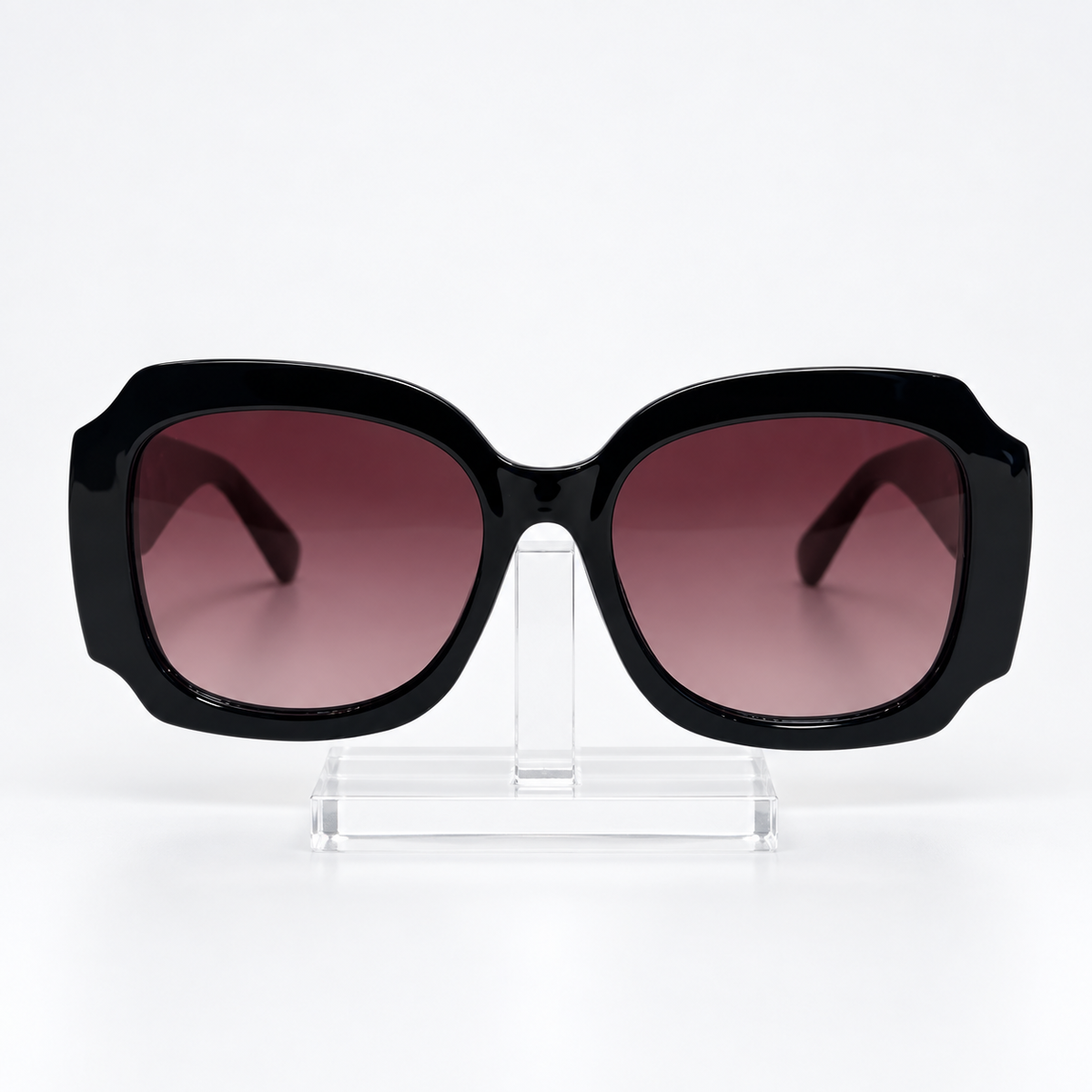 Oversized square sunglasses with a glossy black frame and gradient brown-tinted lenses, displayed on a clear acrylic stand against a white background.