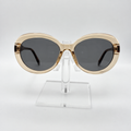 Oversized oval sunglasses with a gold-tone frame and dark gray lenses, displayed on a clear acrylic stand against a light gray background.