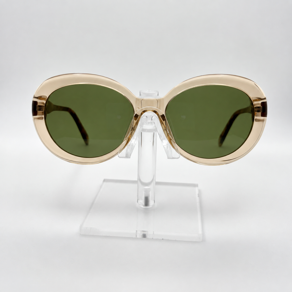 Oversized oval sunglasses with a translucent champagne-gold frame and dark green lenses, displayed on a clear acrylic stand against a light gray background.