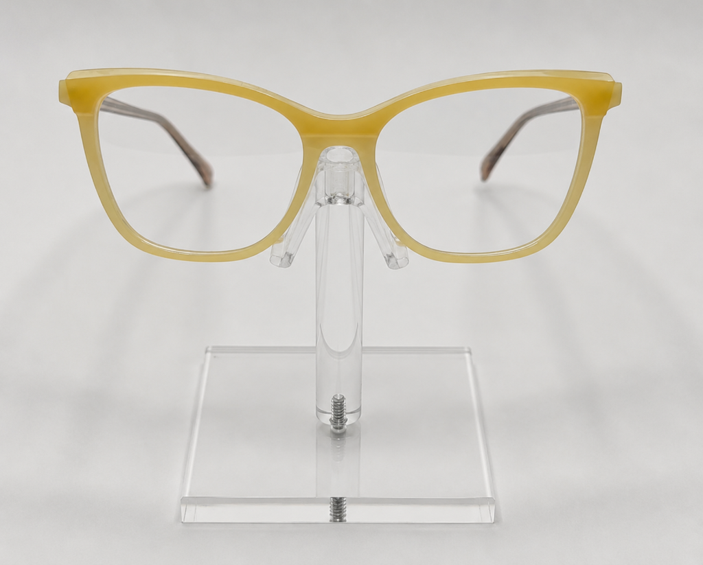 Yellow cat-eye eyeglasses displayed on a clear acrylic stand against a light gray background.