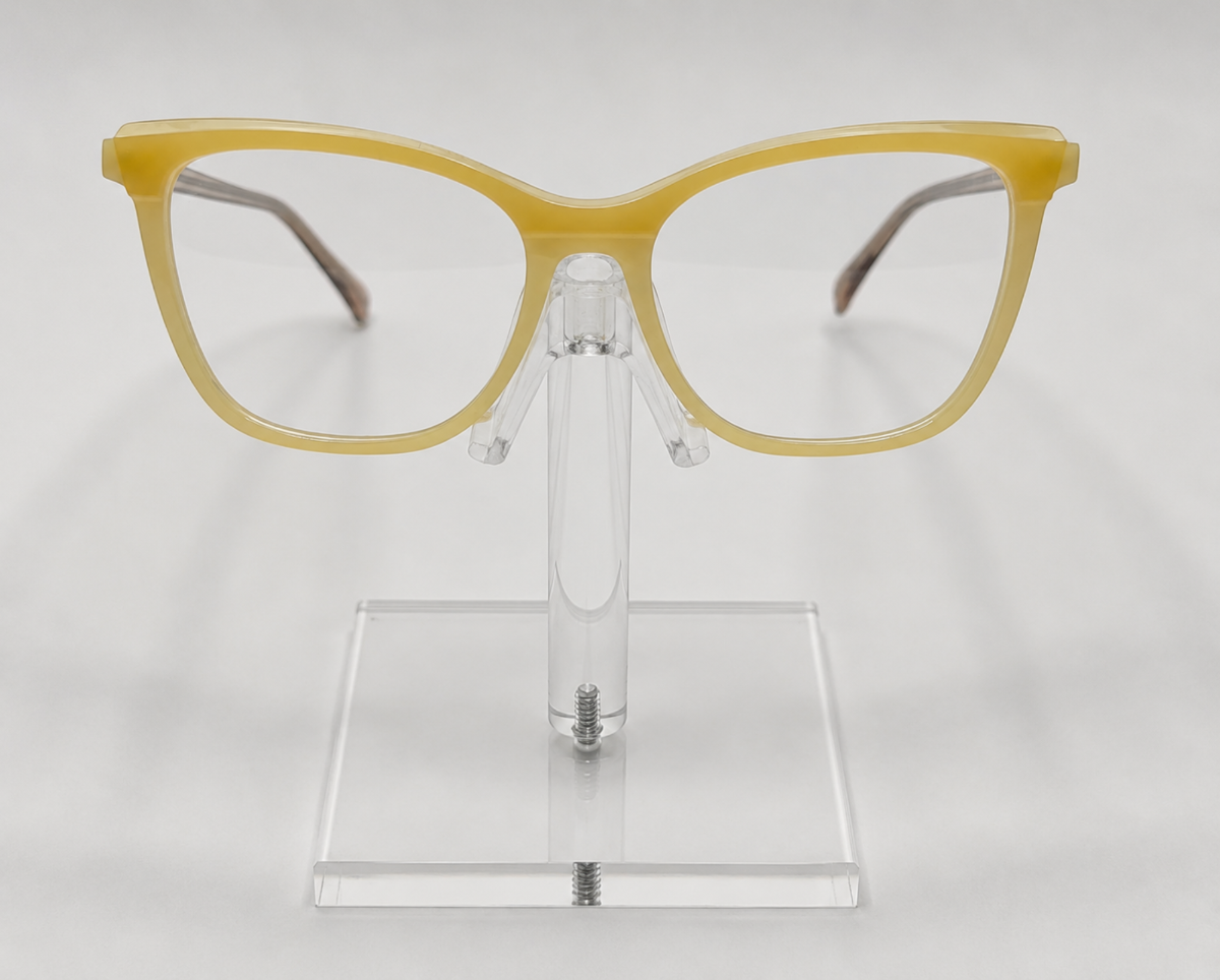 Yellow cat-eye eyeglasses displayed on a clear acrylic stand against a light gray background.