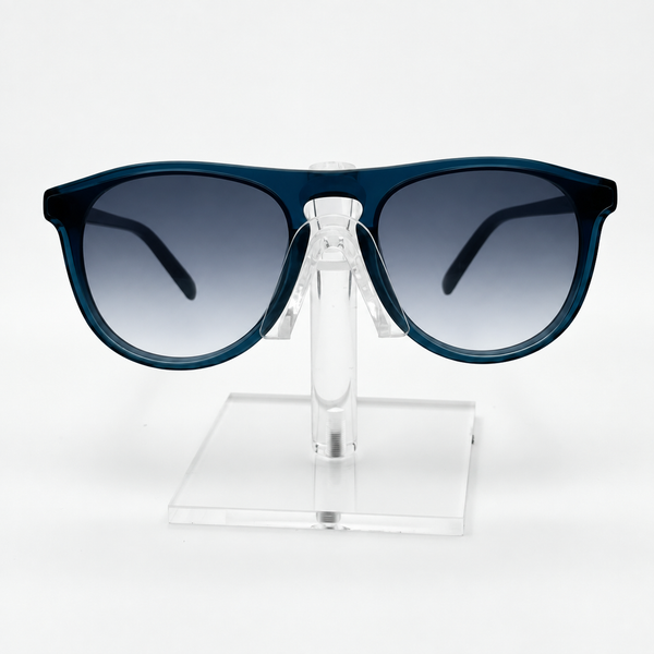 A pair of sunglasses with a translucent dark blue frame and gradient gray lenses, displayed on a clear acrylic stand against a white background.