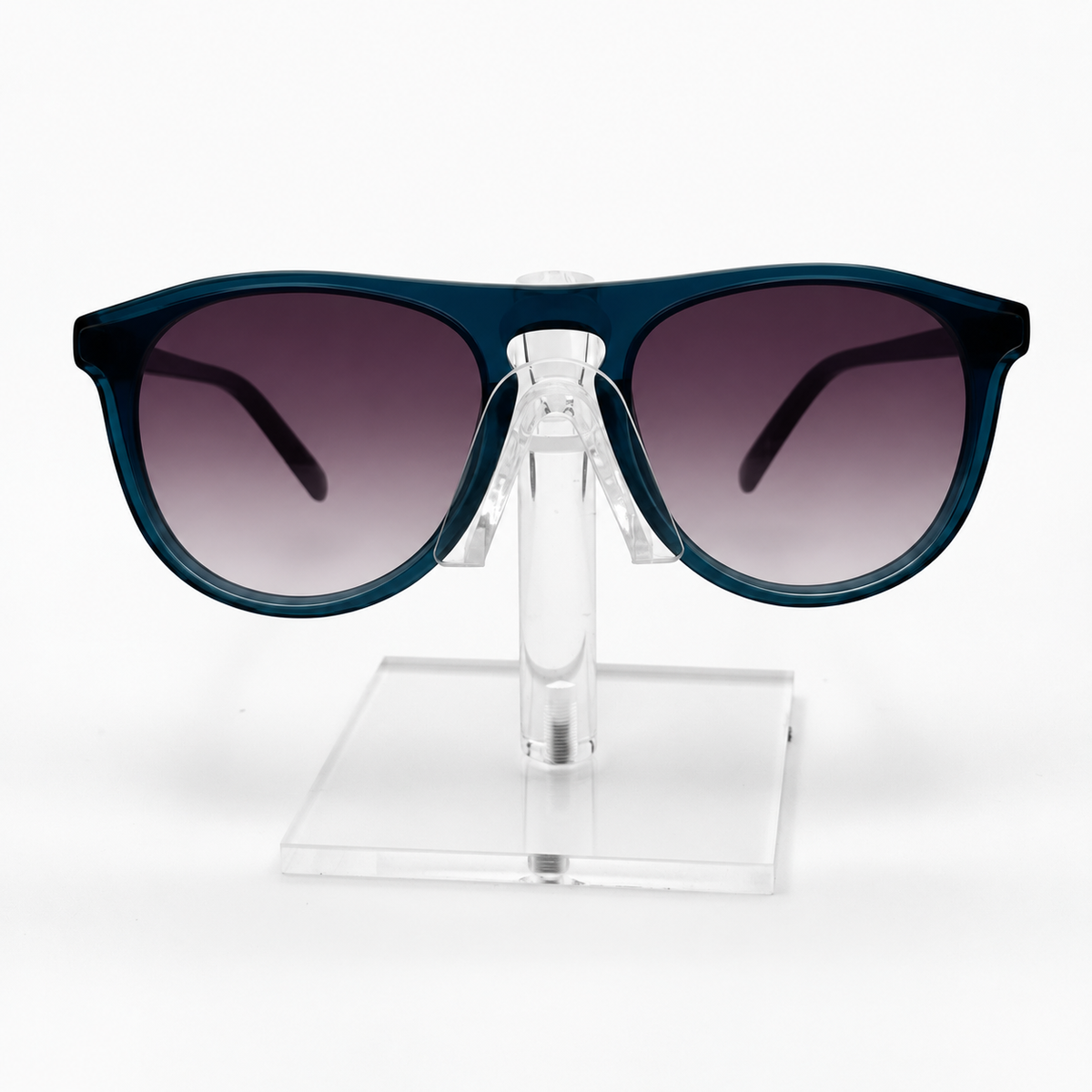 A pair of sunglasses with a dark teal-blue frame and gradient gray lenses, displayed on a clear acrylic stand against a white background.