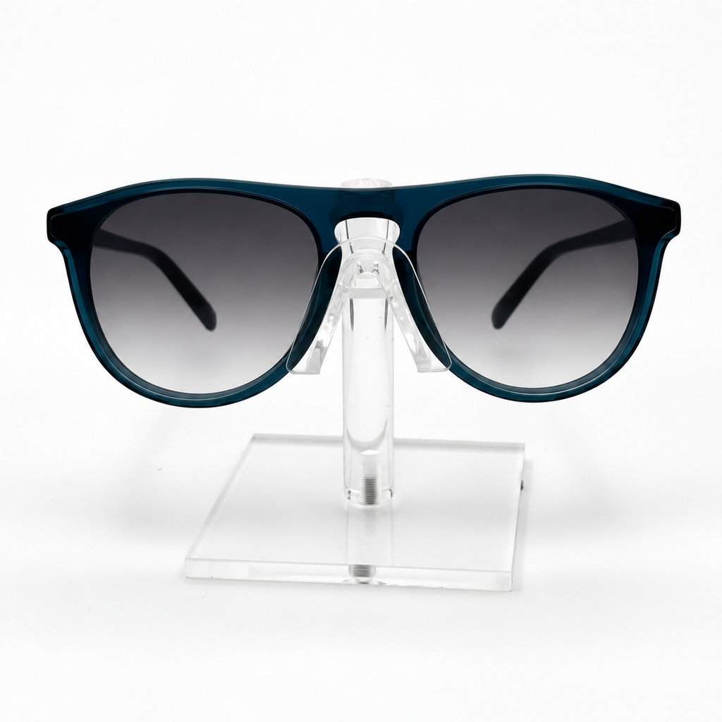 A pair of sunglasses with a dark teal-blue frame and gradient gray lenses, displayed on a clear acrylic stand against a white background.