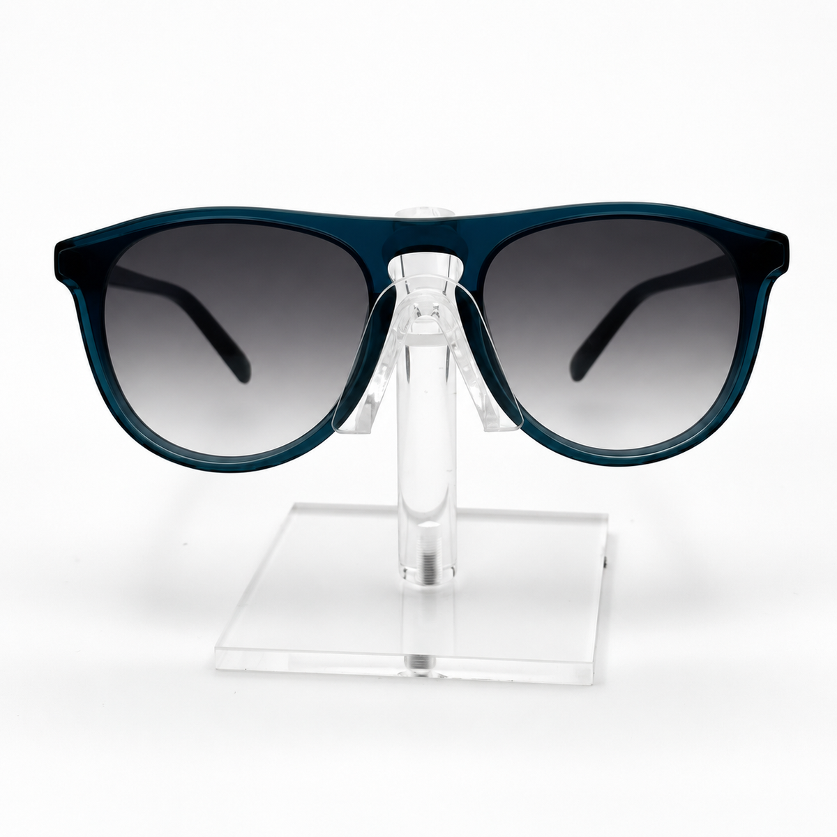 A pair of sunglasses with a dark teal-blue frame and gradient gray lenses, displayed on a clear acrylic stand against a white background.