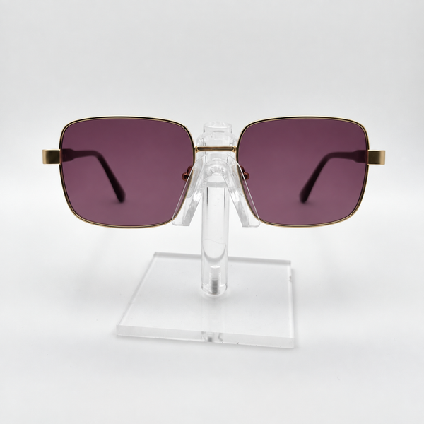 Square sunglasses with dark purple lenses and gold metal frames, displayed on a clear acrylic stand against a white background.