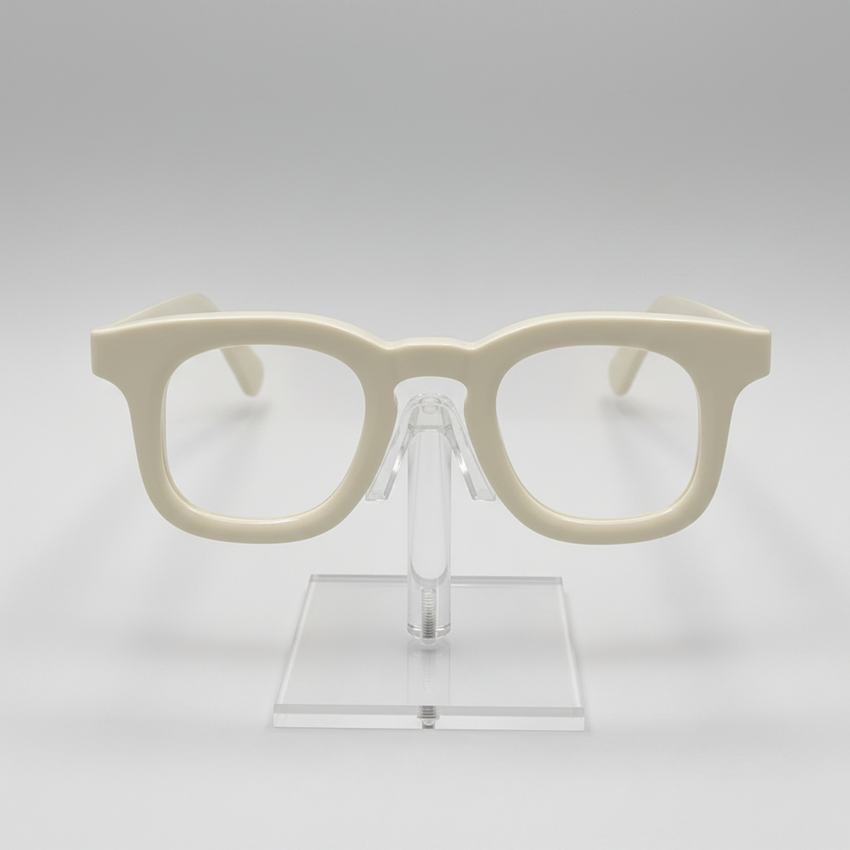 Cream-colored thick-rimmed eyeglasses displayed on a clear acrylic stand against a light gray background.
