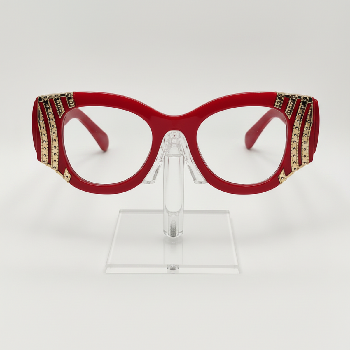 Red cat-eye eyeglasses with gold rhinestone embellishments on the temples, displayed on a clear acrylic stand against a white background.