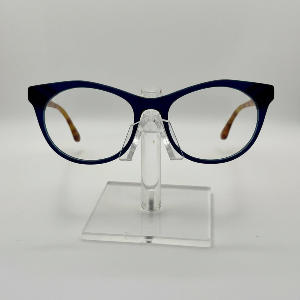 round eyeglasses with a dark navy blue frame and clear lenses, displayed on a transparent acrylic stand against a light gray background.