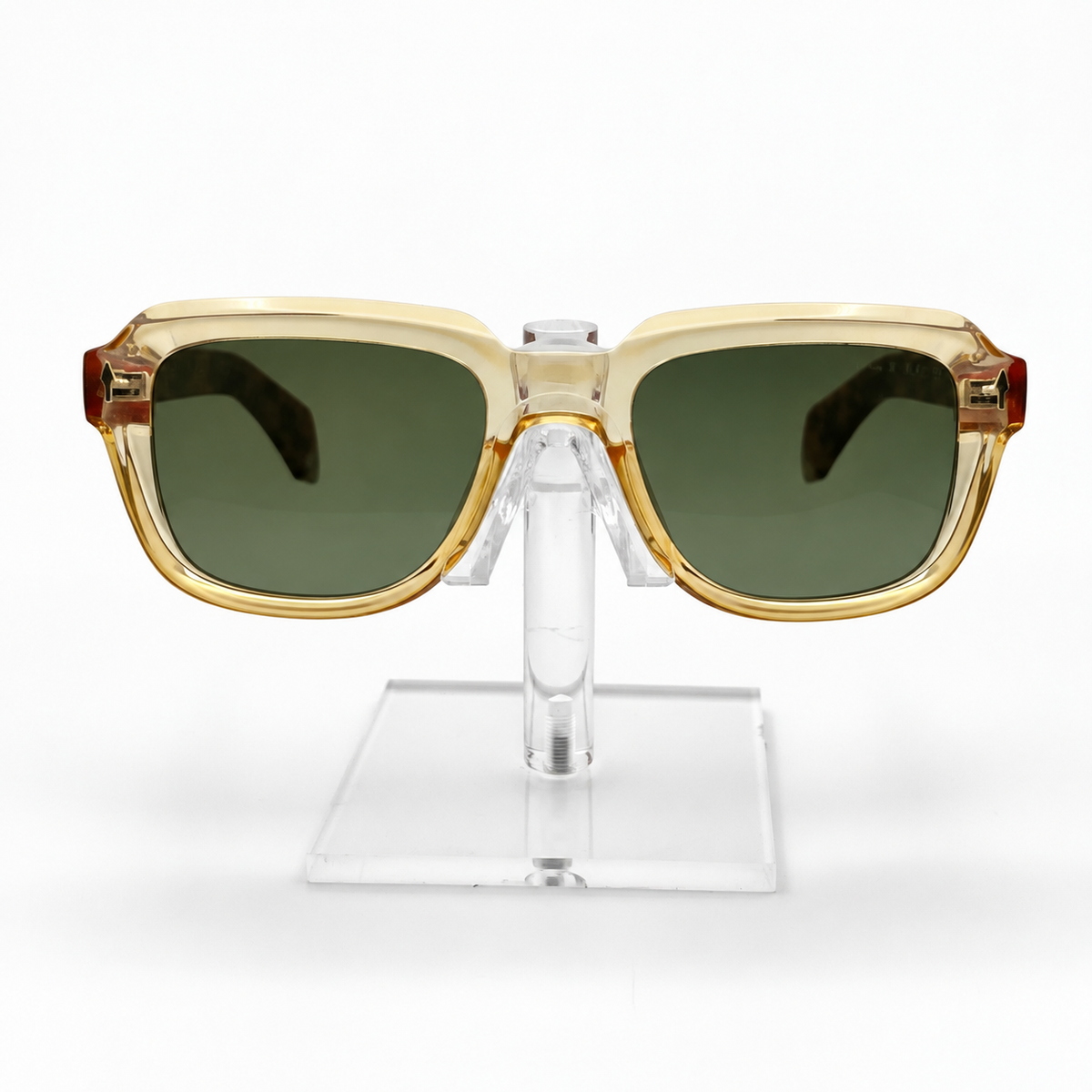 Square sunglasses with a translucent gold acetate frame and dark green lenses, displayed on a clear acrylic stand against a white background.
