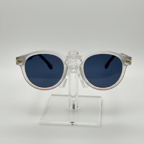 Round sunglasses with a translucent white frame and dark blue lenses, displayed on a clear acrylic stand against a light gray background.