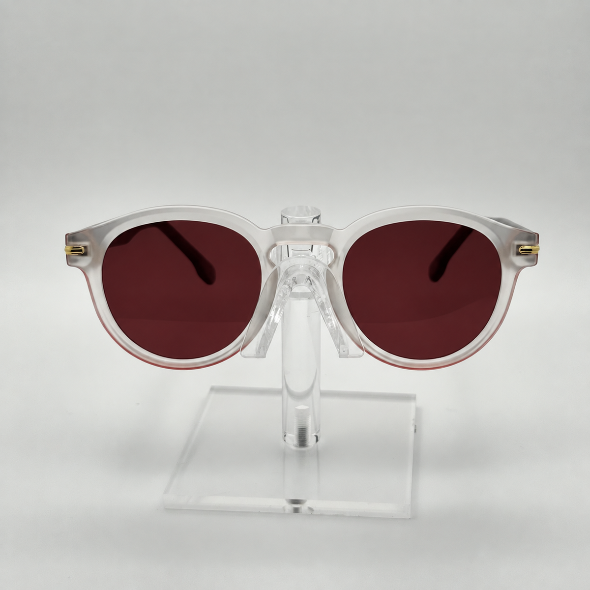 Round sunglasses with translucent white frames and dark reddish-brown lenses, displayed on a clear acrylic stand against a light gray background.