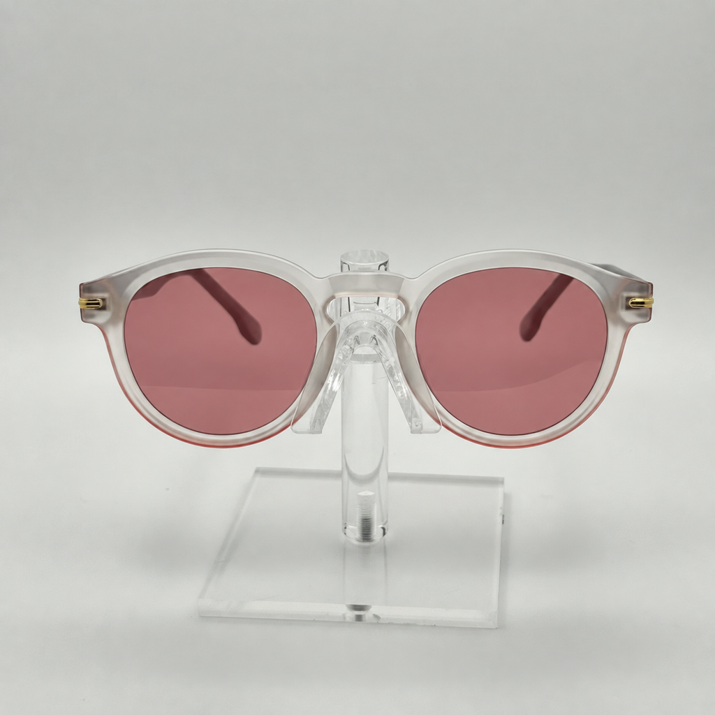 Round sunglasses with translucent white frames and pink lenses, displayed on a clear acrylic stand against a light gray background.