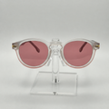 Round sunglasses with translucent white frames and pink lenses, displayed on a clear acrylic stand against a light gray background.