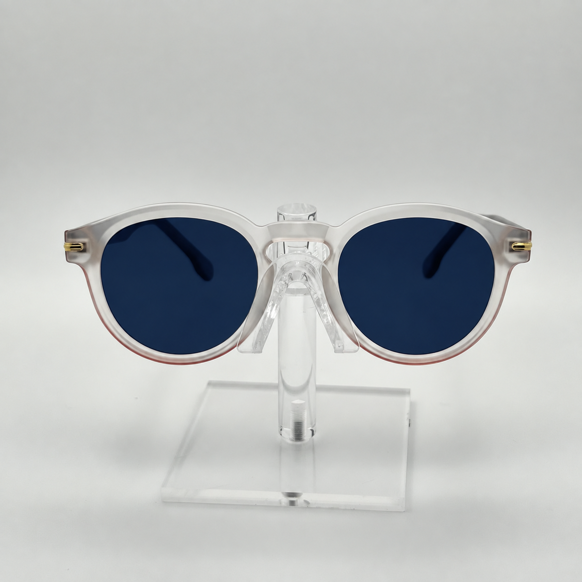 Round sunglasses with translucent white frames and dark blue lenses, displayed on a clear acrylic stand against a light gray background.