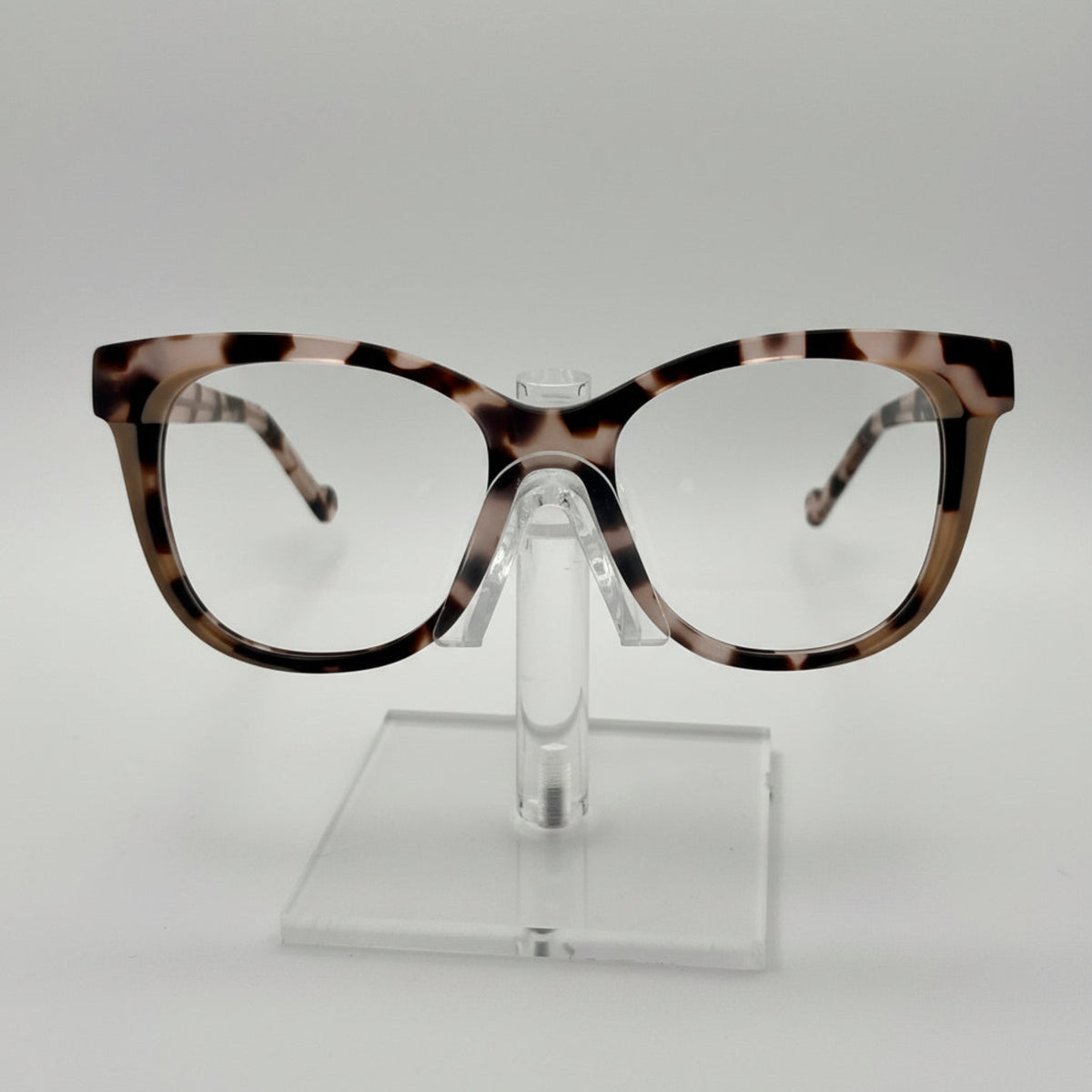 Tortoiseshell eyeglasses on a clear stand against a white background
