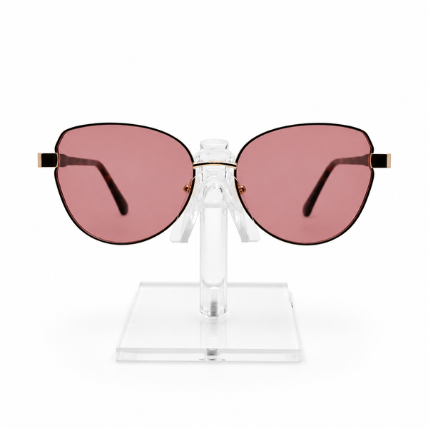 Oversized cat-eye sunglasses with dusty rose pink lenses and gold metal frames, displayed on a clear acrylic stand against a white background.