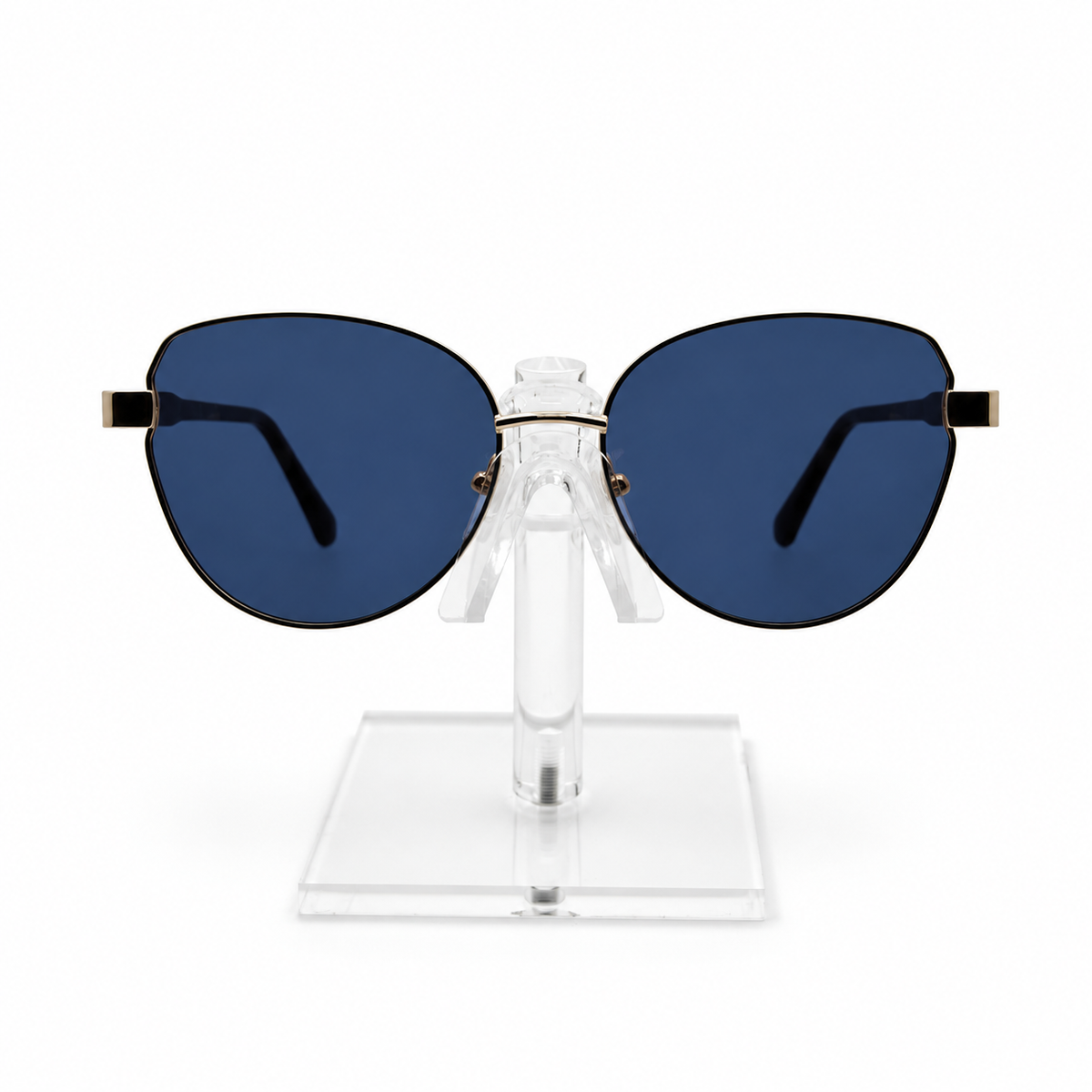 Oversized cat-eye sunglasses with dark blue lenses and gold metal temples, displayed on a clear acrylic stand against a white background.