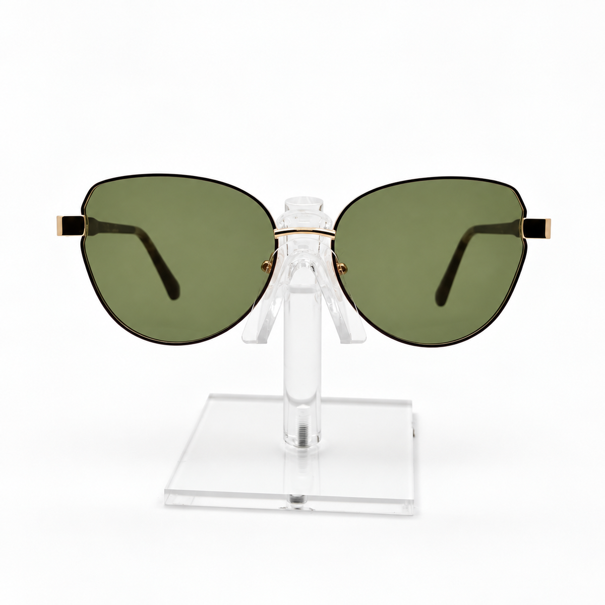 Oversized cat-eye sunglasses with olive green lenses and gold metal accents, displayed on a clear acrylic stand against a white background.