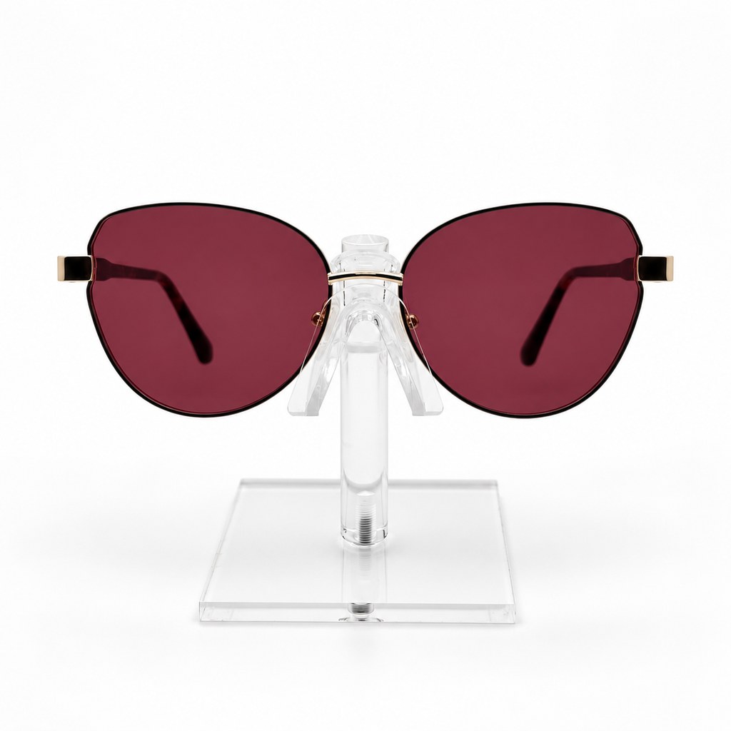 Oversized cat-eye sunglasses with dark red lenses and gold metal temples, displayed on a clear acrylic stand against a white background.