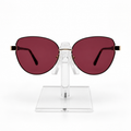 Oversized cat-eye sunglasses with dark red lenses and gold metal temples, displayed on a clear acrylic stand against a white background.