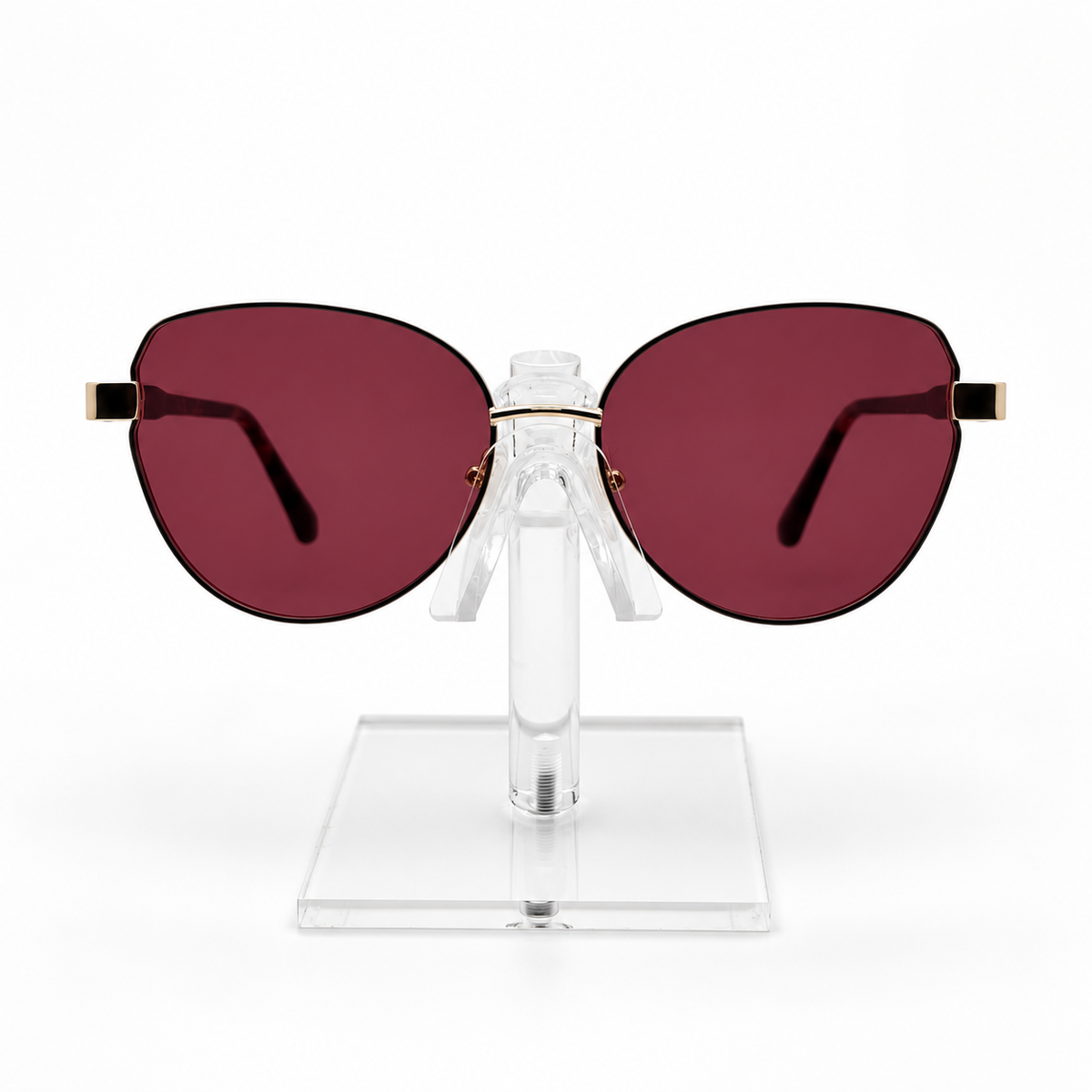 Oversized cat-eye sunglasses with dark red lenses and gold metal temples, displayed on a clear acrylic stand against a white background.