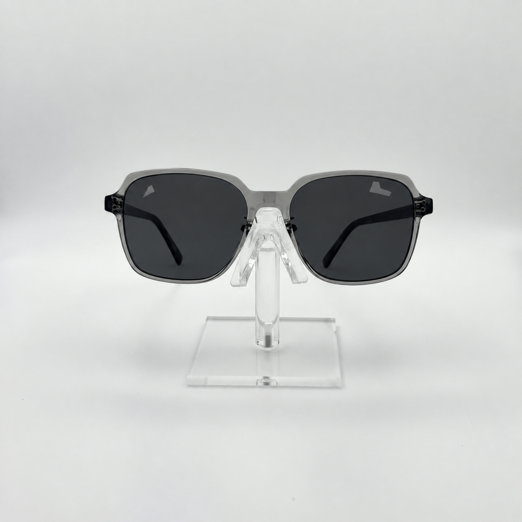Square sunglasses with a translucent gray frame and dark gray lenses, displayed on a clear acrylic stand against a light gray background.