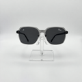 Square sunglasses with a translucent gray frame and dark gray lenses, displayed on a clear acrylic stand against a light gray background.