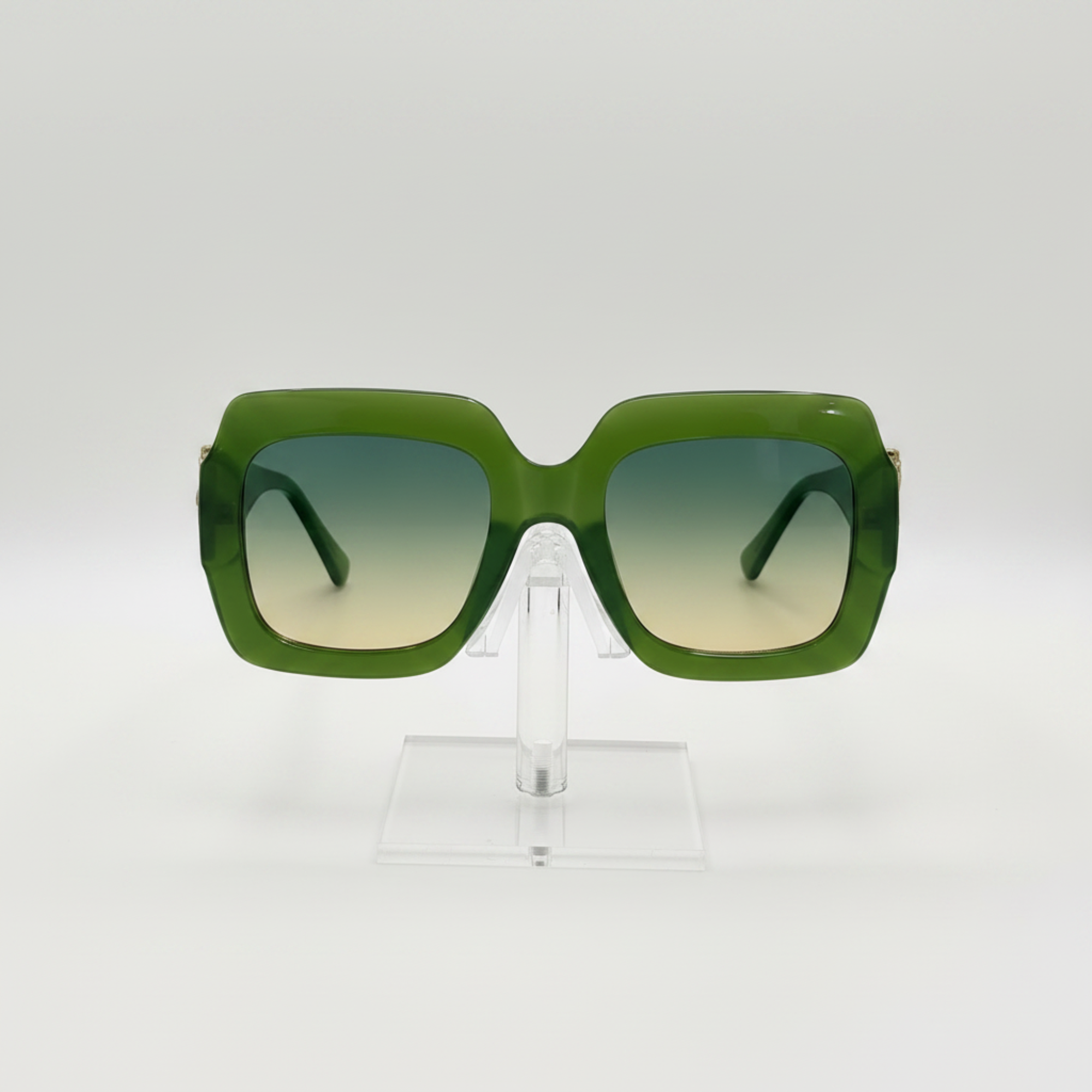 Green oversized square sunglasses with gradient lenses, displayed on a clear acrylic stand against a white background.