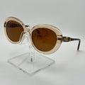 Gold-framed sunglasses with brown lenses on a clear stand against a white background