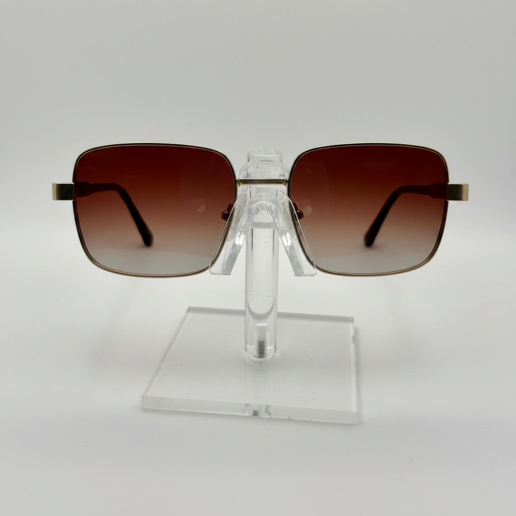 Square aviator-style sunglasses with brown gradient lenses and gold metal frames, displayed on a clear acrylic stand against a white background.