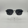 Oversized square sunglasses with a translucent smoky gray frame and dark gray lenses, displayed on a clear acrylic stand against a light gray background.