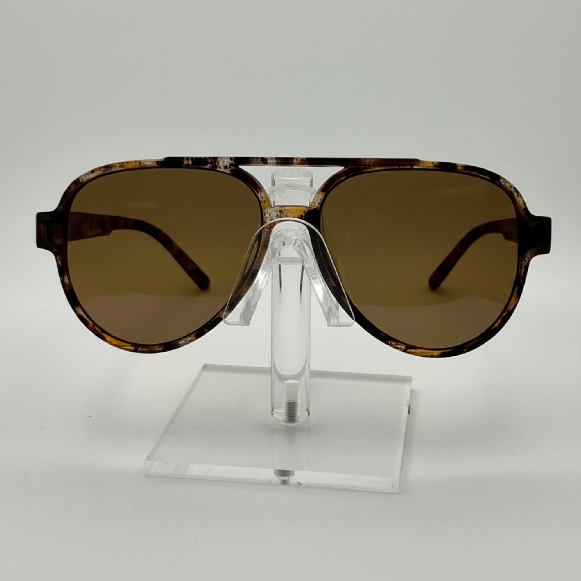 A pair of oversized aviator-style sunglasses with a tortoiseshell patterned frame and brown tinted lenses, displayed on a clear acrylic stand against a white background.