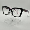 Black square eyeglasses with a tortoiseshell pattern on the temples, displayed on a clear acrylic stand against a light gray background.