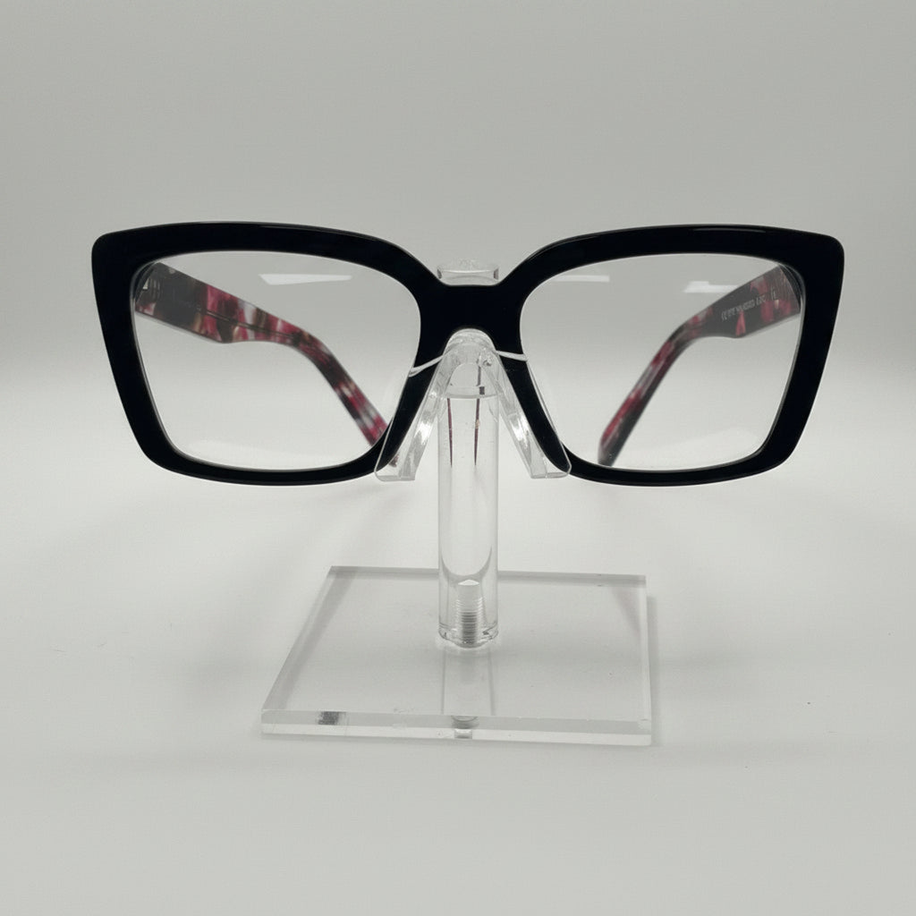 Black cat-eye eyeglasses with clear lenses and patterned inner temples, displayed on a clear acrylic stand against a white background.