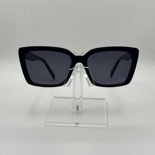 Black square sunglasses with dark lenses displayed on a clear acrylic stand against a light gray background.