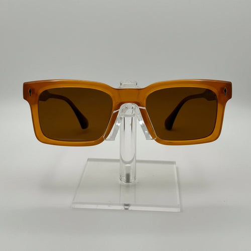 Rectangular sunglasses with translucent amber-brown frames and dark brown lenses, displayed on a clear acrylic stand against a light gray background.