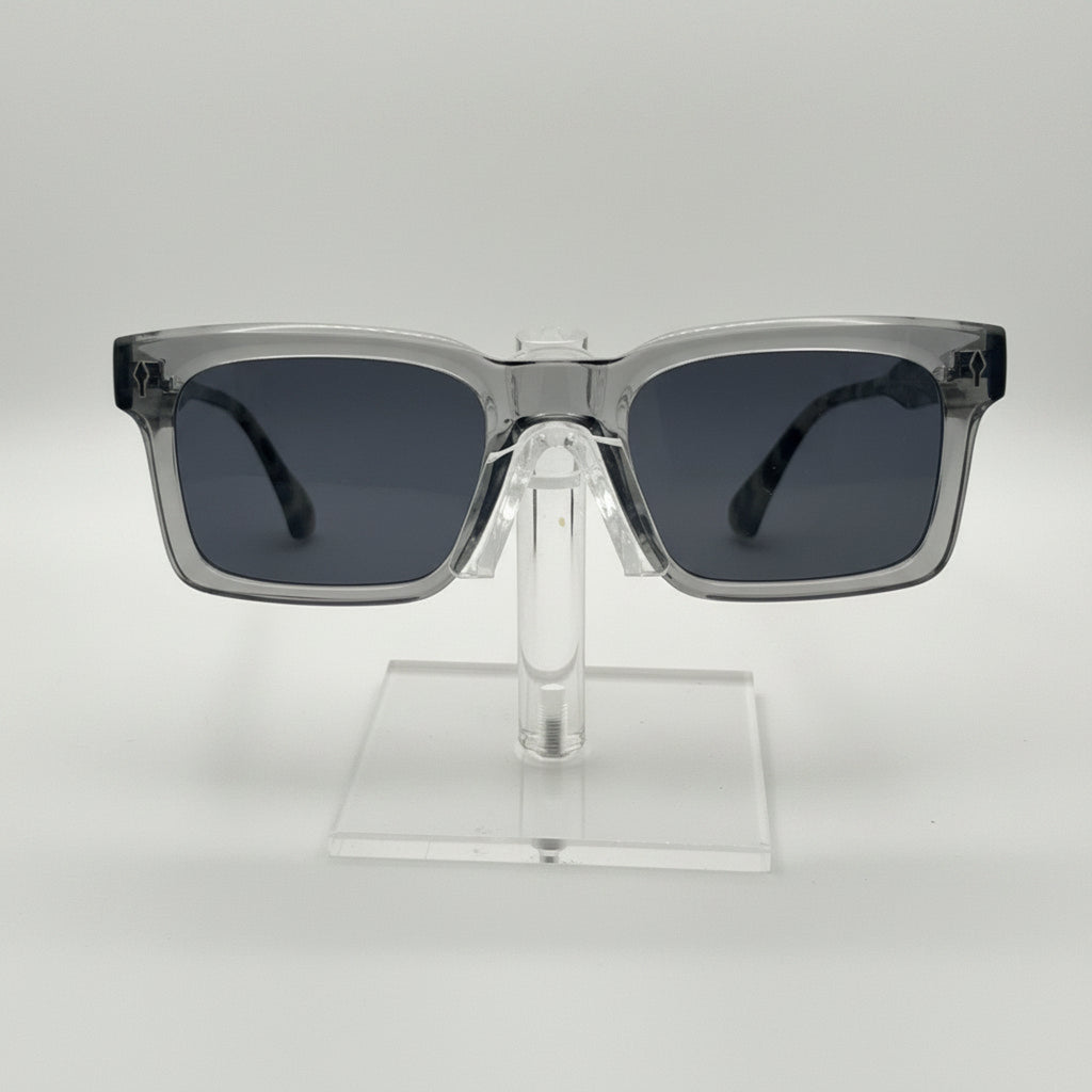 Square sunglasses with a translucent smoky gray frame and dark gray lenses, displayed on a clear acrylic stand against a light gray background.