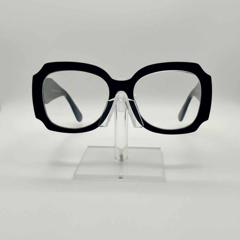 Oversized square eyeglasses with a thick black frame and clear lenses, displayed on a transparent acrylic stand against a light gray background.