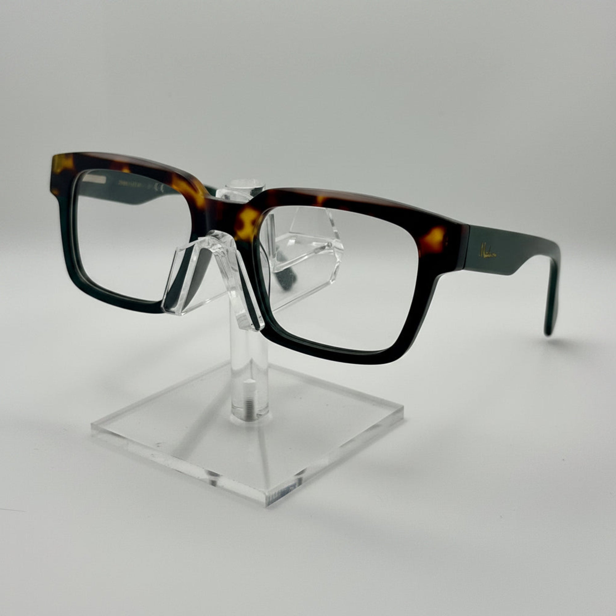 Rectangular eyeglasses with a glossy black and tortoiseshell acetate frame, displayed on a clear acrylic stand against a light gray background.