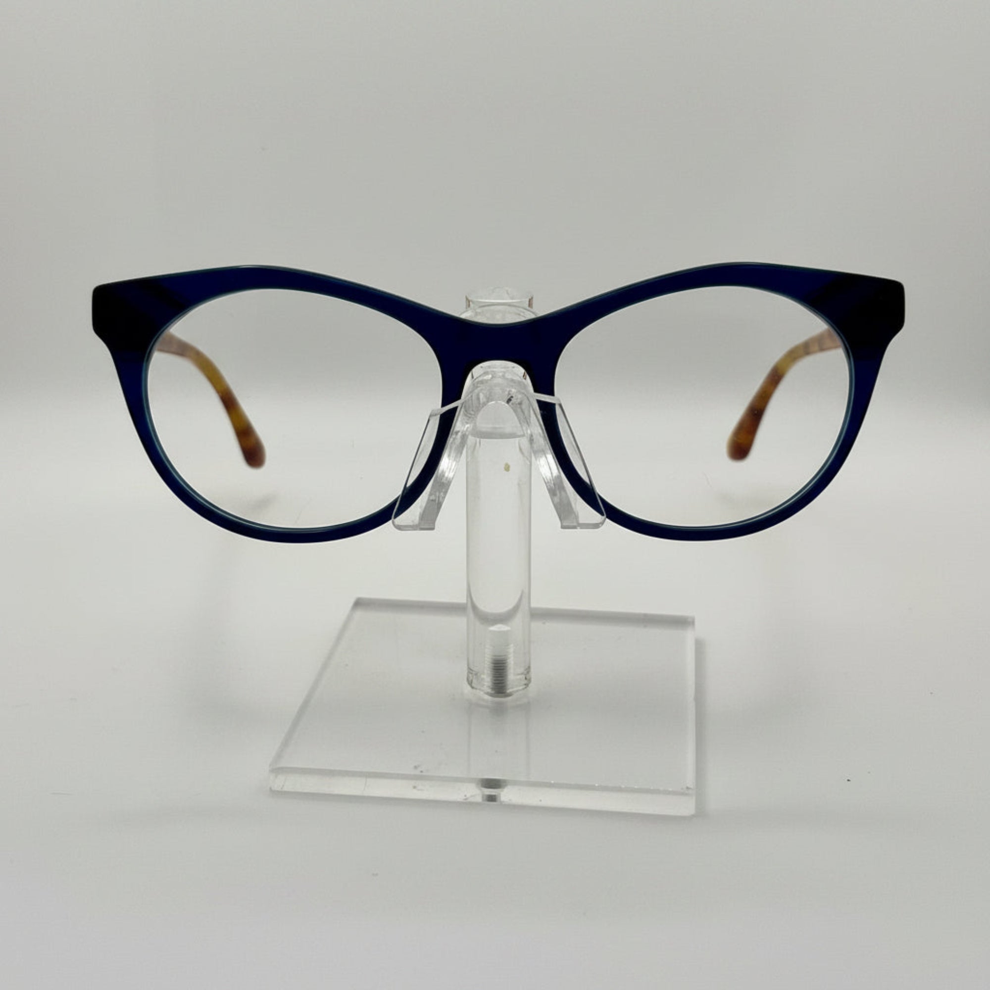 round eyeglasses with a dark navy blue frame and clear lenses, displayed on a transparent acrylic stand against a light gray background.