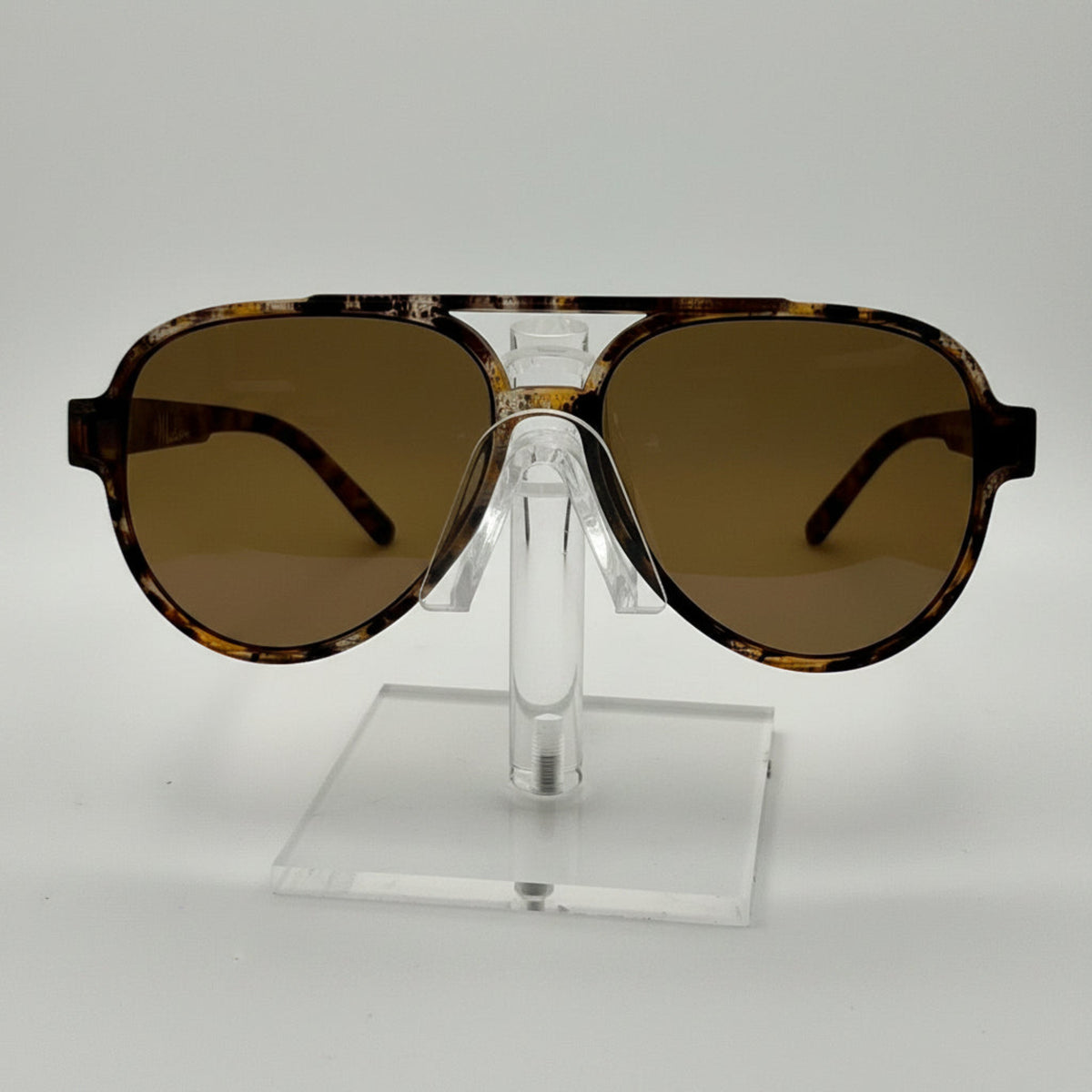 A pair of oversized aviator-style sunglasses with a tortoiseshell patterned frame and brown tinted lenses, displayed on a clear acrylic stand against a white background.