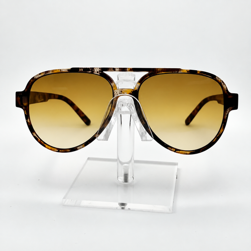A pair of oversized aviator-style sunglasses with a tortoiseshell frame and gradient amber lenses, displayed on a clear acrylic stand against a white background.