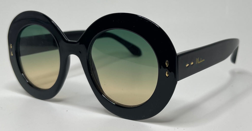 Oversized round sunglasses with a glossy black frame and gradient green-to-gold tinted lenses, featuring gold-tone rivets and a visible 'Mikimoto' logo on the temple arm.